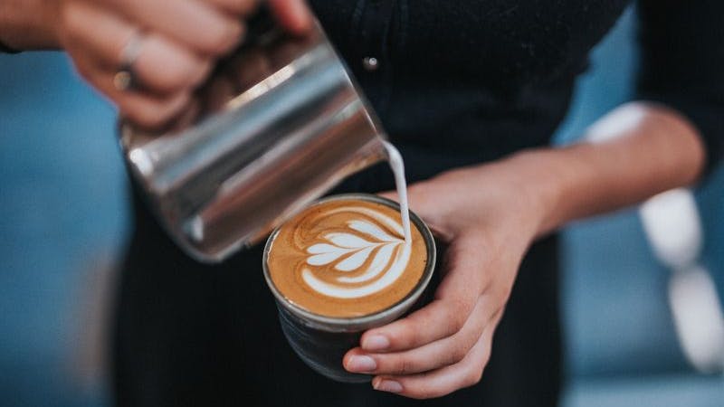 Café Petit. Auf dem Bild sieht man eine Person, die Milch in eine Kaffeetasse kippt.
